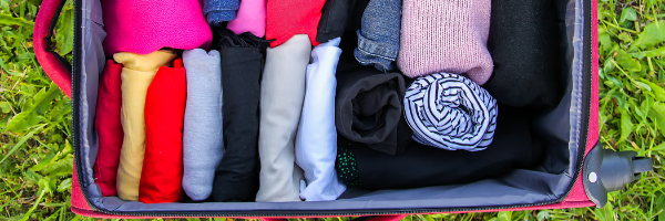 pink suitcase in grass filled with clothes